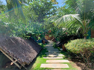A sun-dappled stone pathway winding through lush tropical greenery leading to a tranquil spa pavilion.