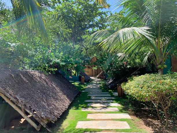 A sun-dappled stone pathway winding through lush tropical greenery leading to a tranquil spa pavilion.
