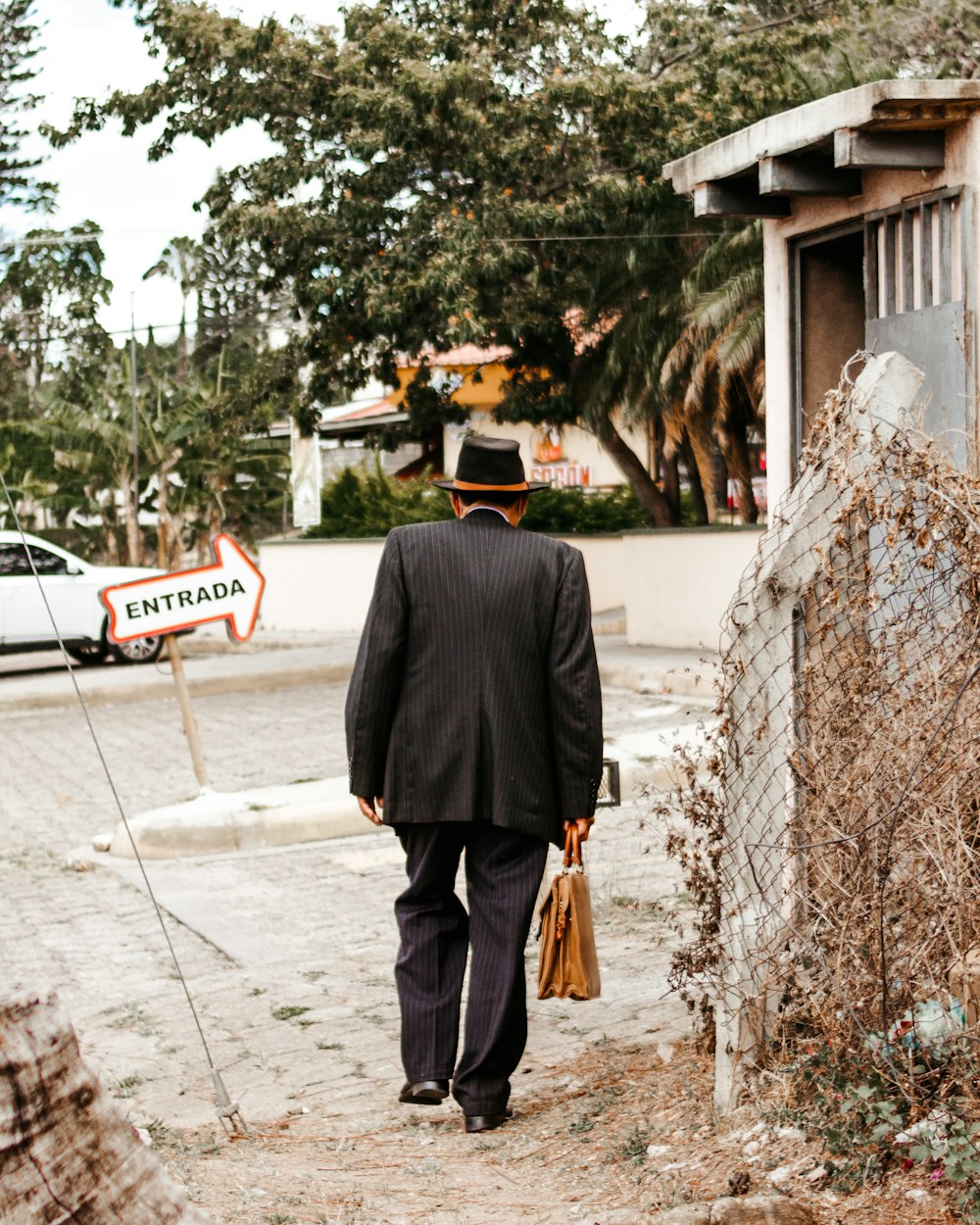 man in black suit jacket and black pants standing near brown wooden bench during daytime