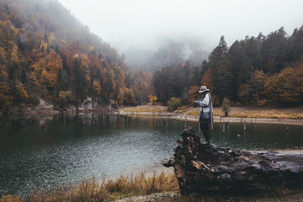 man in white and black jacket standing on rock near river during daytime