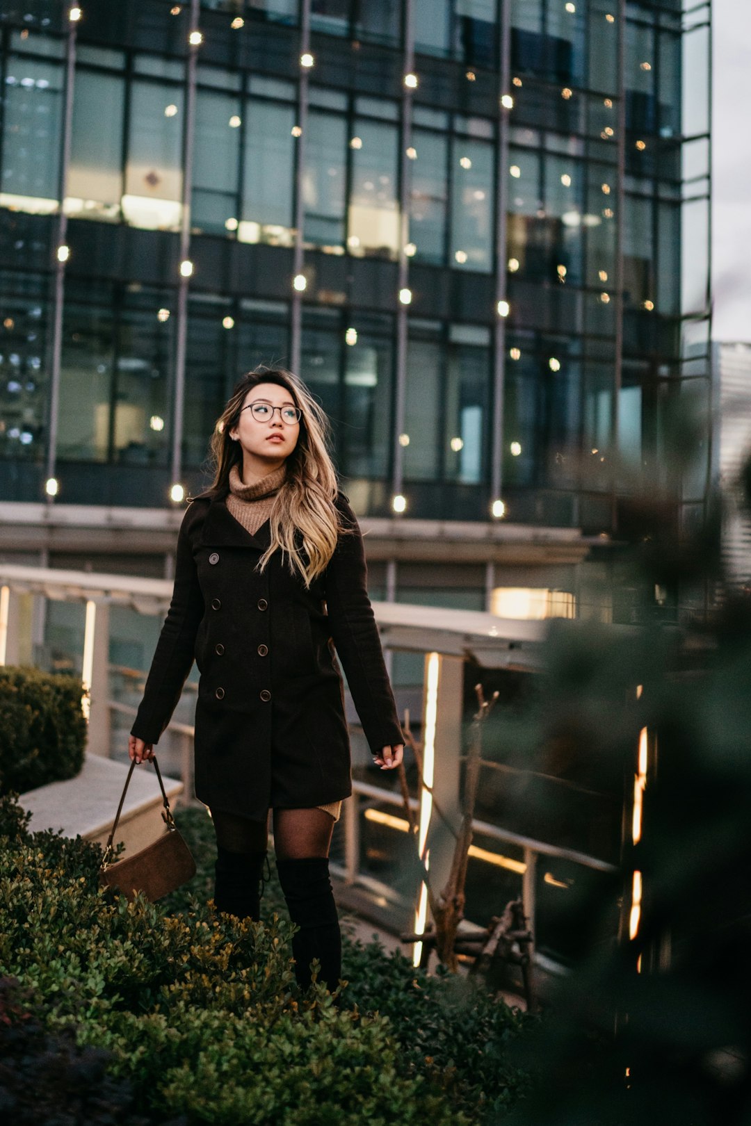 woman in black jacket standing near glass building during night time