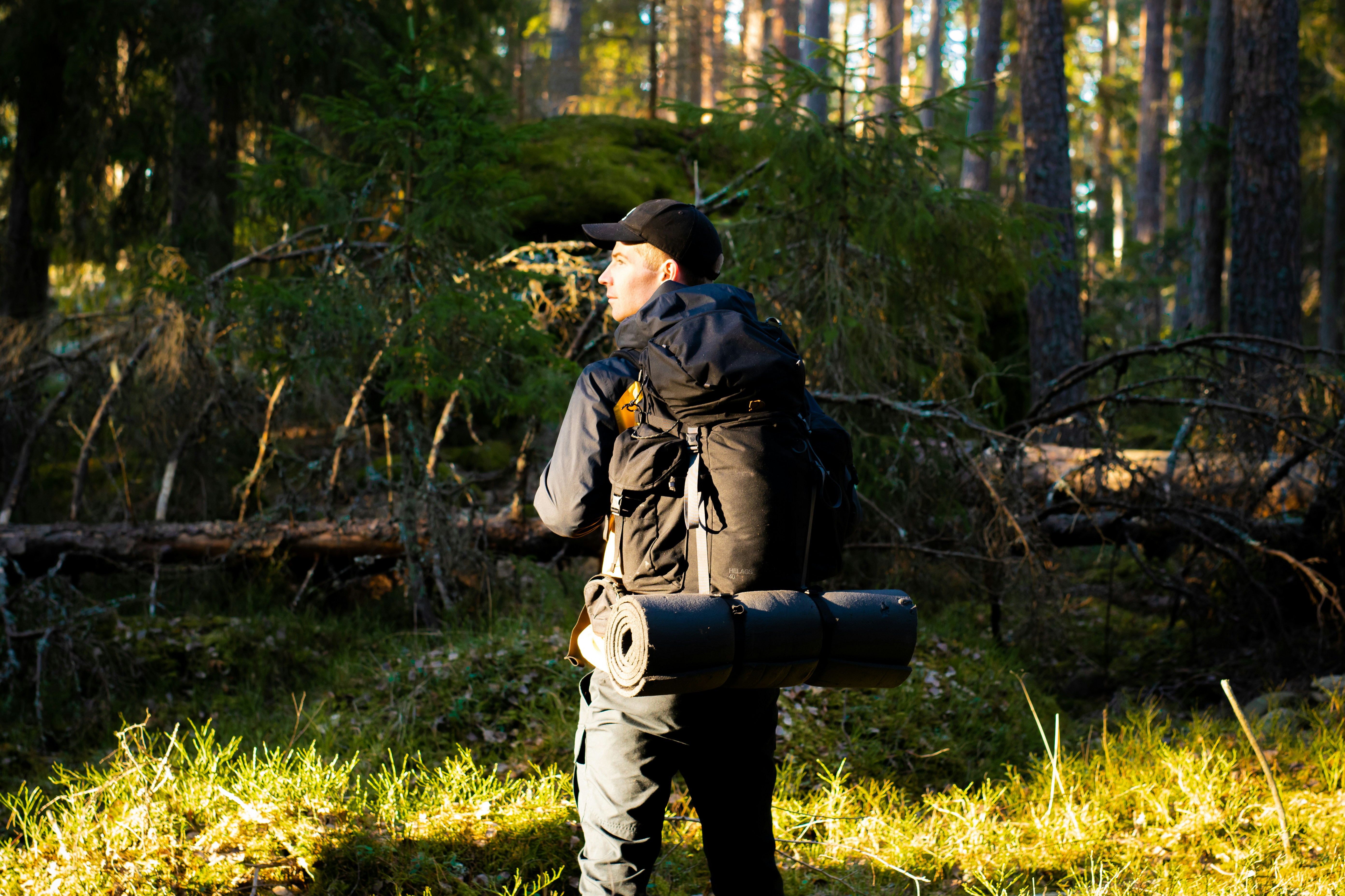 man in black jacket and black pants carrying black backpack standing on green grass field during