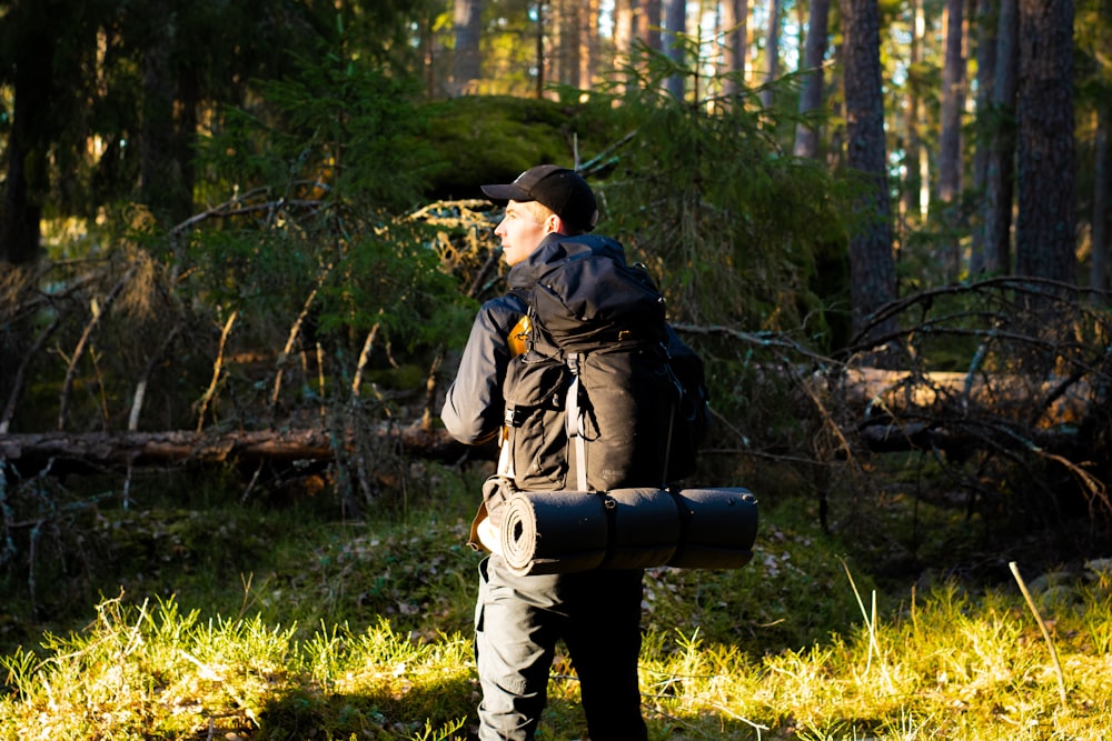 man in black jacket and black pants carrying black backpack standing on green grass field during