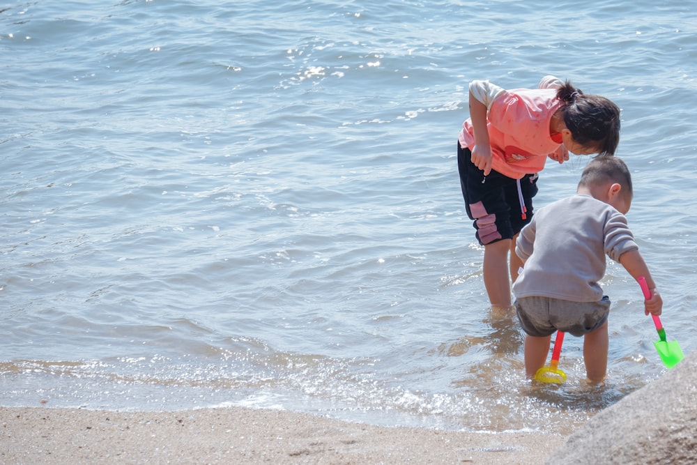 man in red shirt carrying child in white shirt on beach during daytime