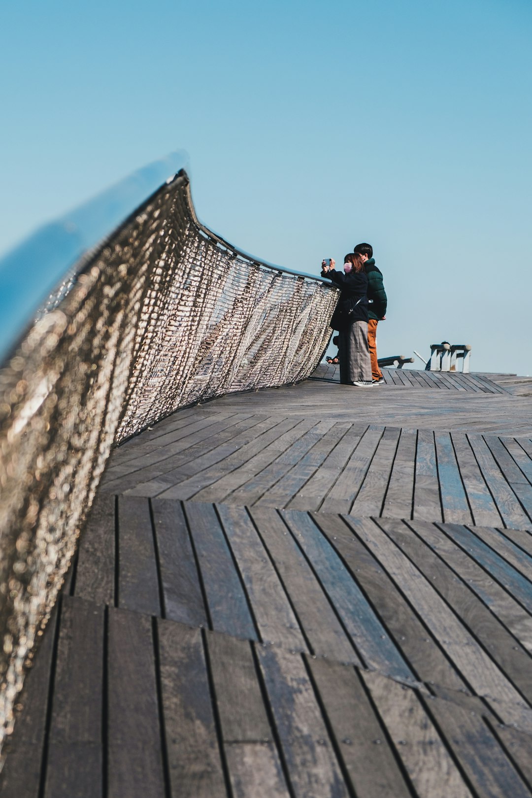 man in black jacket and blue denim jeans standing on brown wooden dock during daytime