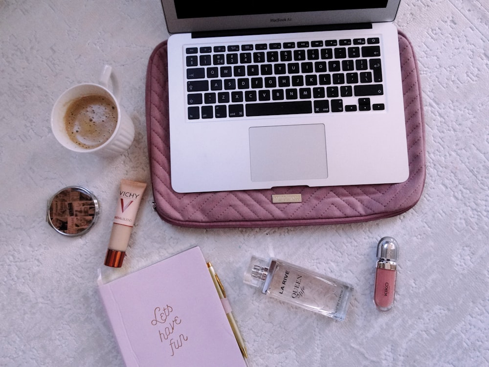 macbook pro beside pink leather case and white ceramic mug on brown wooden table