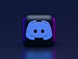 A 3D-style block with a blue logo in the center, set against a dark background. The logo resembles a game controller with two rounded edges and two circles on the front. The block has a subtle gradient, transitioning from dark to purple on its sides.