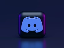 A 3D-style block with a blue logo in the center, set against a dark background. The logo resembles a game controller with two rounded edges and two circles on the front. The block has a subtle gradient, transitioning from dark to purple on its sides.