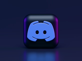 A 3D-style block with a blue logo in the center, set against a dark background. The logo resembles a game controller with two rounded edges and two circles on the front. The block has a subtle gradient, transitioning from dark to purple on its sides.
