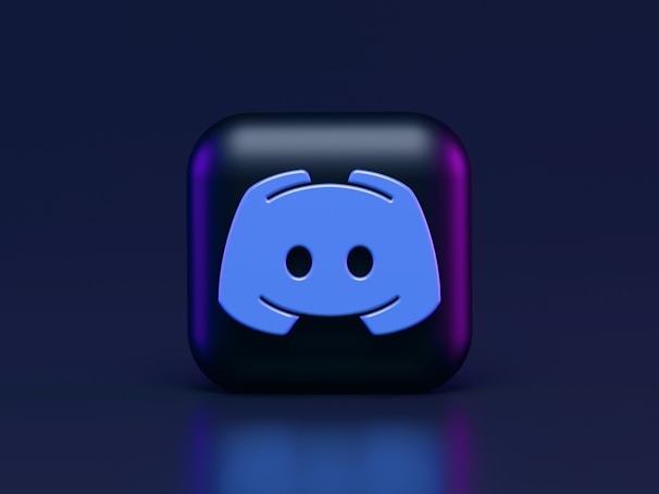A 3D-style block with a blue logo in the center, set against a dark background. The logo resembles a game controller with two rounded edges and two circles on the front. The block has a subtle gradient, transitioning from dark to purple on its sides.