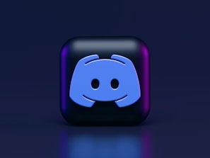A 3D-style block with a blue logo in the center, set against a dark background. The logo resembles a game controller with two rounded edges and two circles on the front. The block has a subtle gradient, transitioning from dark to purple on its sides.