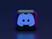 A 3D-style block with a blue logo in the center, set against a dark background. The logo resembles a game controller with two rounded edges and two circles on the front. The block has a subtle gradient, transitioning from dark to purple on its sides.