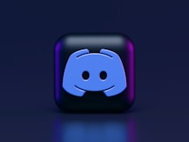 A 3D-style block with a blue logo in the center, set against a dark background. The logo resembles a game controller with two rounded edges and two circles on the front. The block has a subtle gradient, transitioning from dark to purple on its sides.