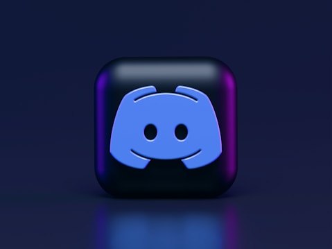 A 3D-style block with a blue logo in the center, set against a dark background. The logo resembles a game controller with two rounded edges and two circles on the front. The block has a subtle gradient, transitioning from dark to purple on its sides.