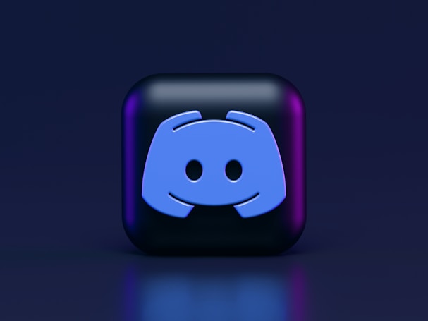 A 3D-style block with a blue logo in the center, set against a dark background. The logo resembles a game controller with two rounded edges and two circles on the front. The block has a subtle gradient, transitioning from dark to purple on its sides.