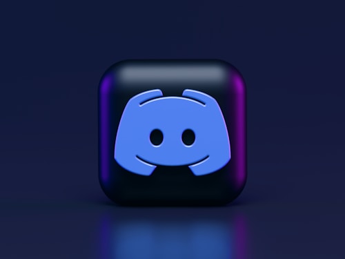A 3D-style block with a blue logo in the center, set against a dark background. The logo resembles a game controller with two rounded edges and two circles on the front. The block has a subtle gradient, transitioning from dark to purple on its sides.