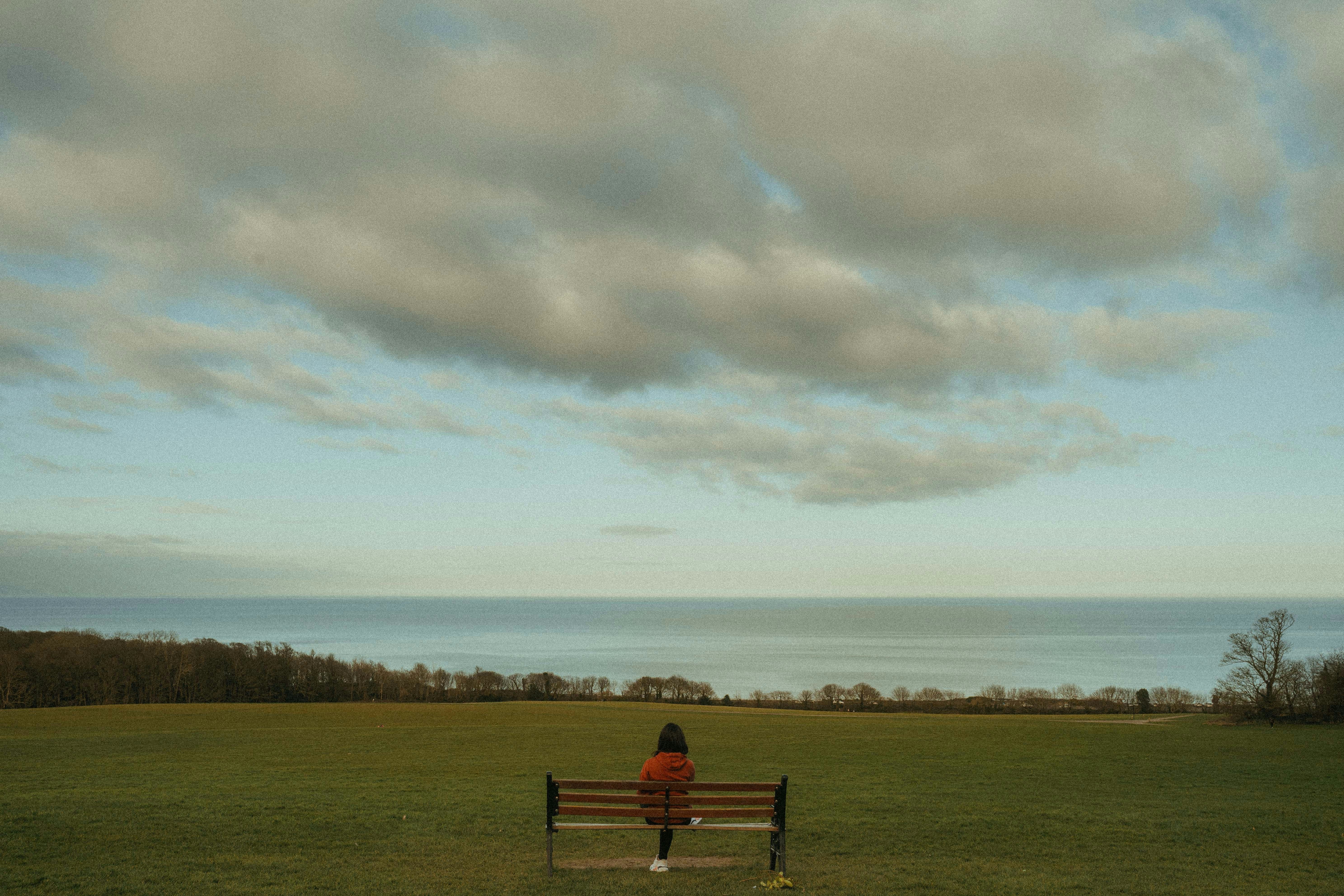 person sitting on bench on green grass field under white clouds during daytime