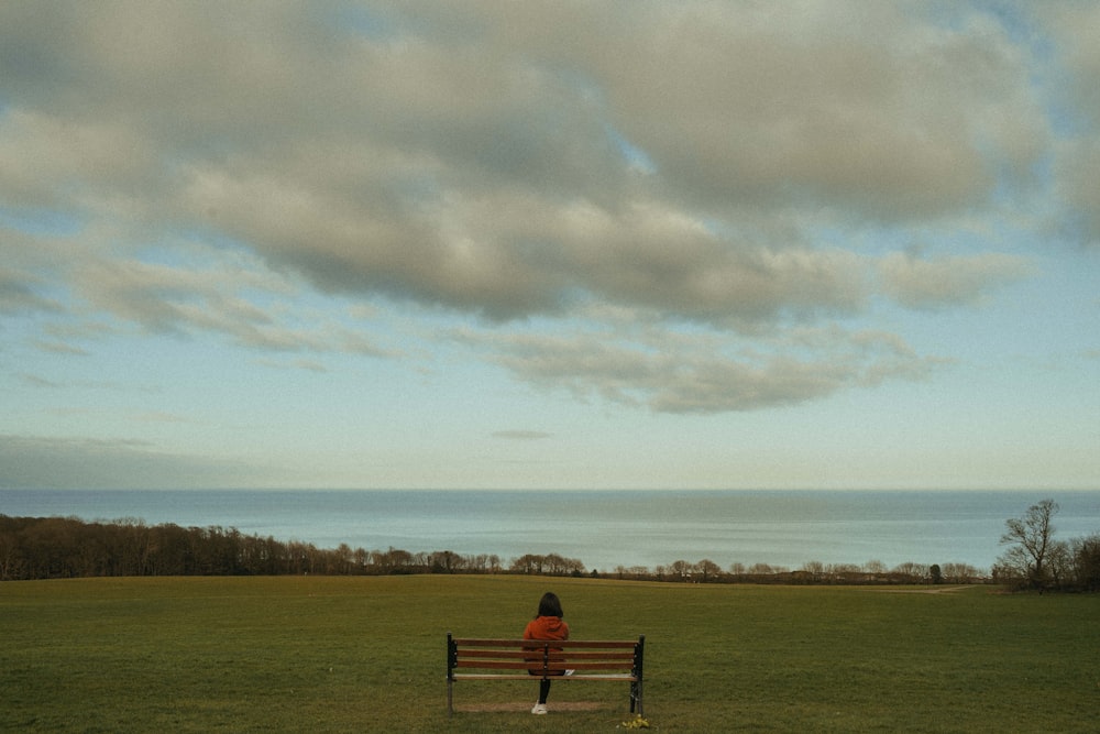 person sitting on bench on green grass field under white clouds during daytime