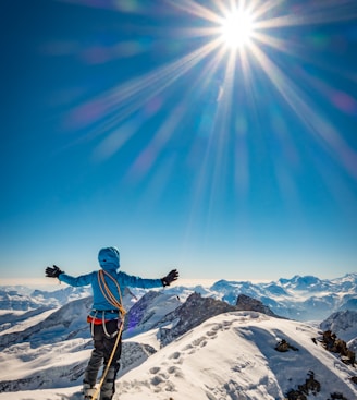 man in blue jacket and black pants standing on snow covered mountain under blue sky during