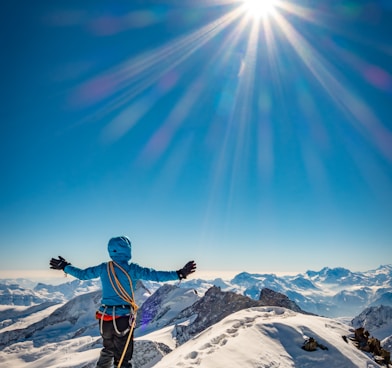 man in blue jacket and black pants standing on snow covered mountain under blue sky during