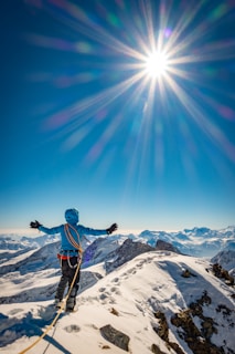 man in blue jacket and black pants standing on snow covered mountain under blue sky during