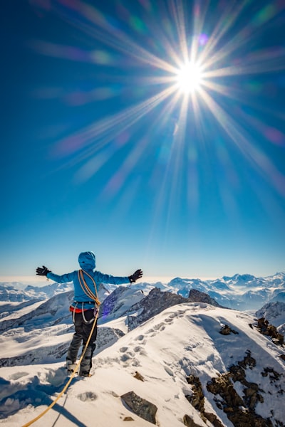 Man in blue jacket and black pants standing on snow covered mountain under blue sky during