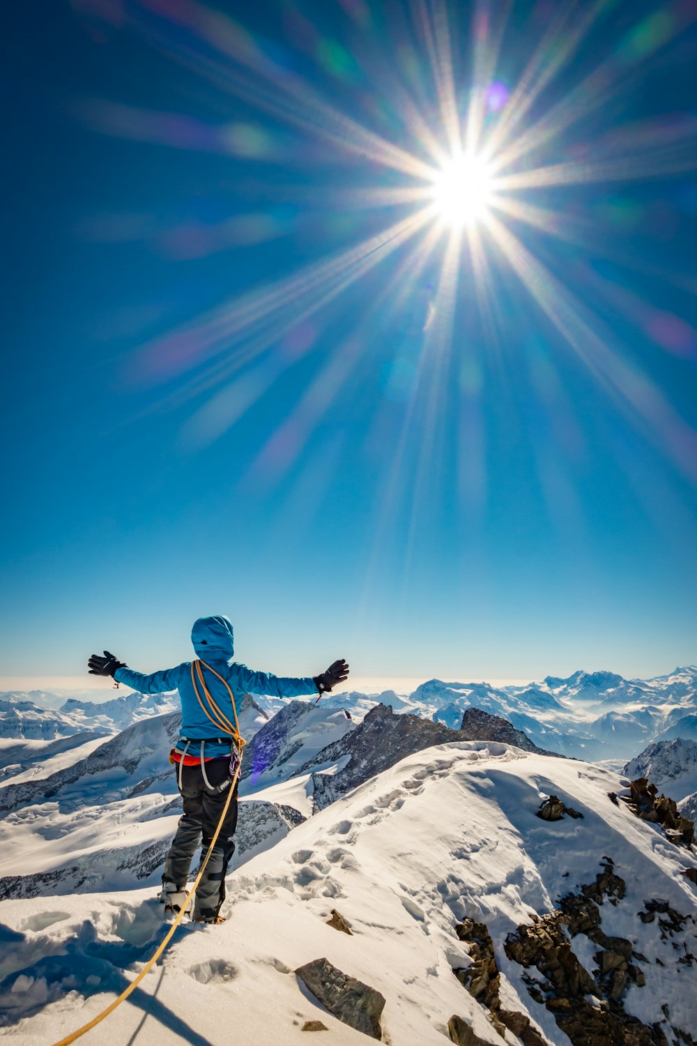Mann in blauer Jacke und schwarzer Hose auf schneebedecktem Berg unter blauem Himmel während