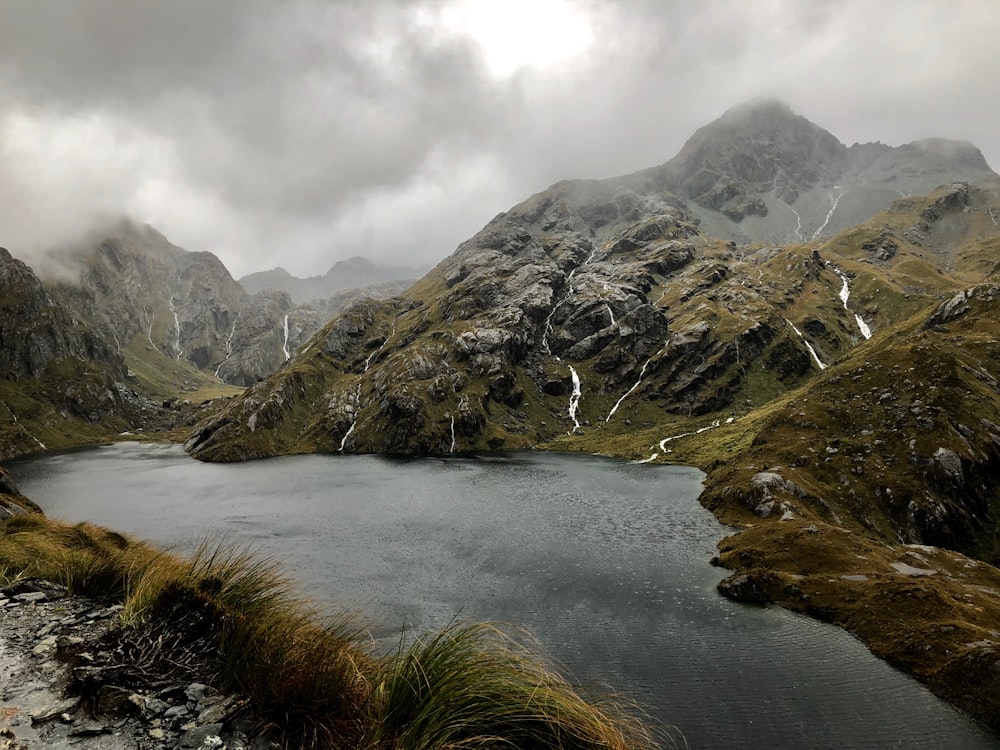 green grass on lake near mountain under cloudy sky during daytime