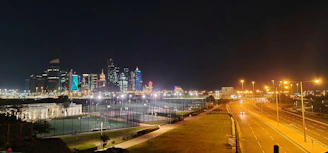 Evening shot of the tournament venue lit up, with players warming up and the city skyline in the background.