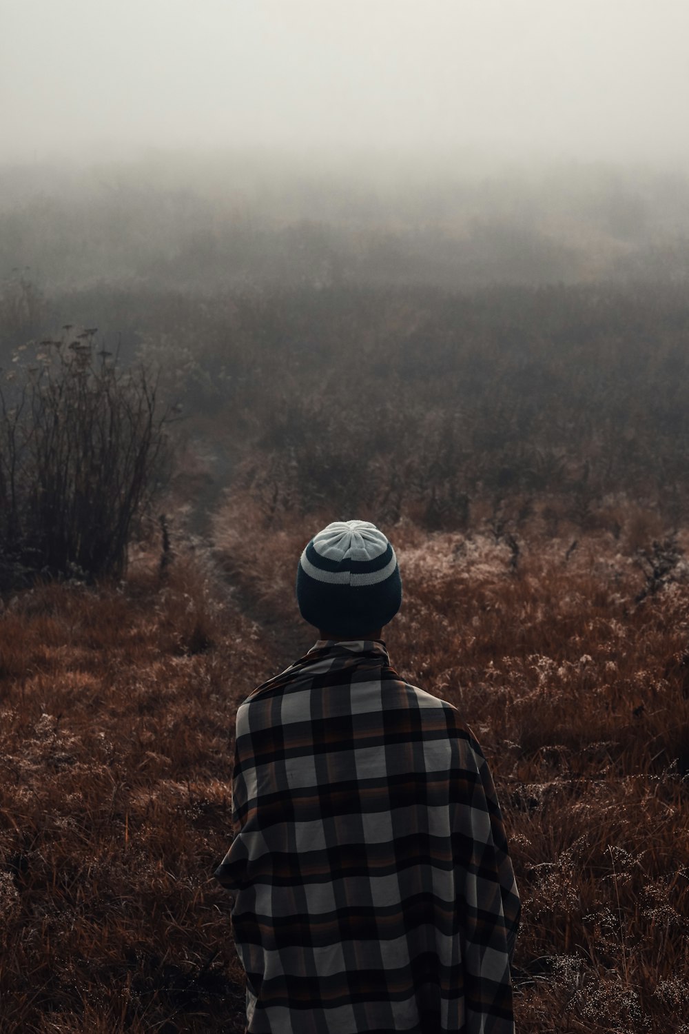 person in black and white plaid shirt wearing black and white cap standing on brown grass