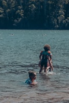 Children playing near the lake, with women watching protectively, embodying community care.
