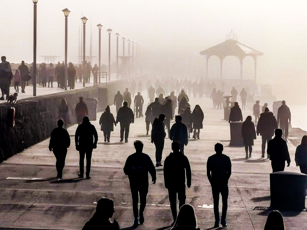 silhouette di persone che camminano sul marciapiede di cemento grigio durante il giorno