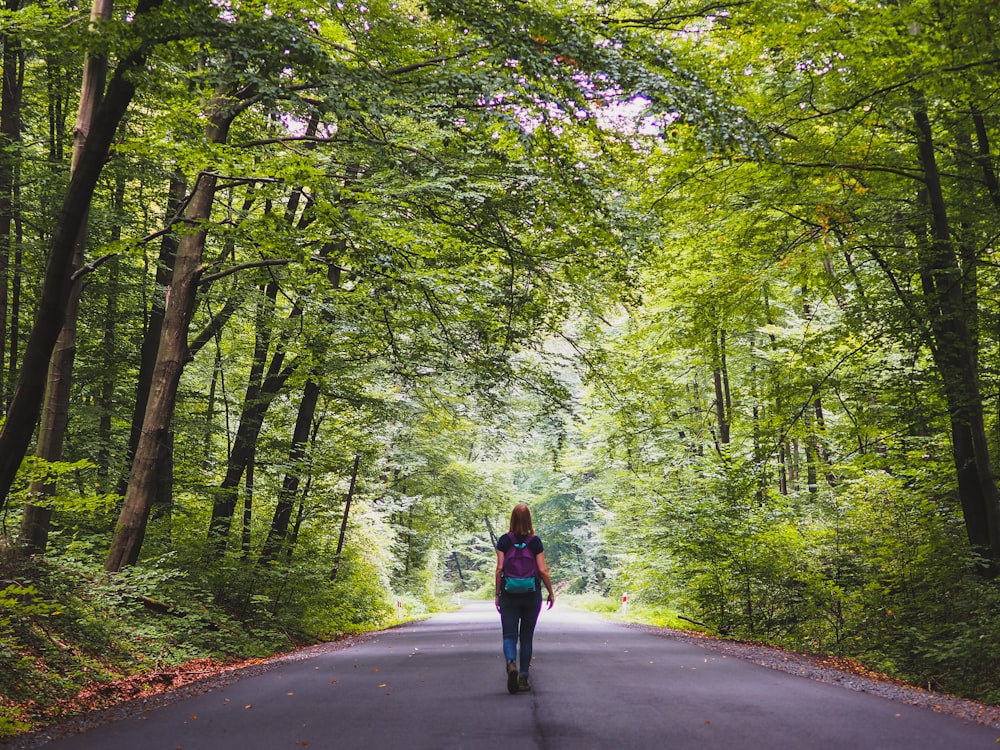 woman in red jacket walking on road between trees during daytime