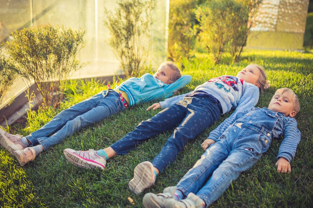2 boys lying on green grass field during daytime