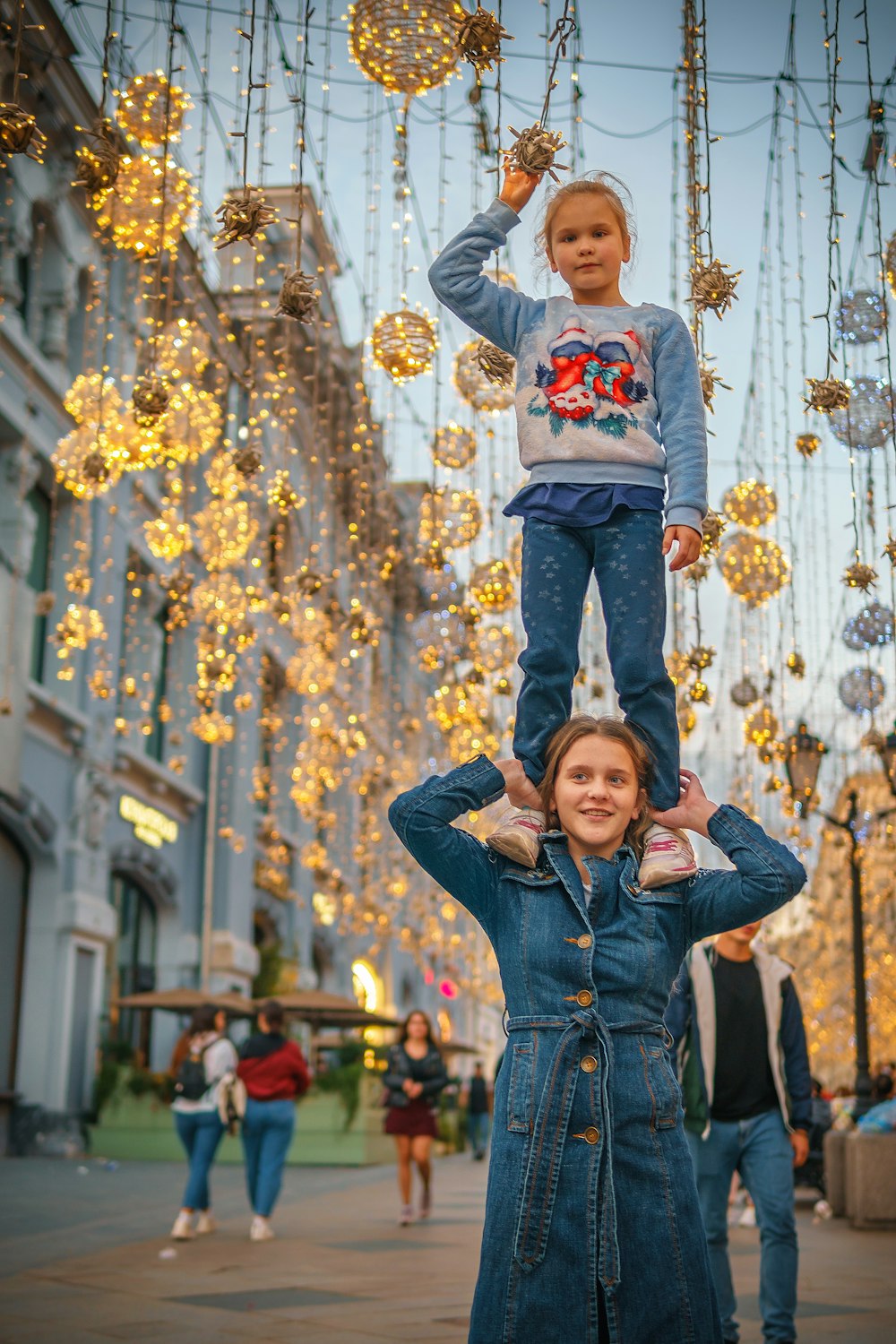 girl in blue denim jacket standing beside yellow string lights