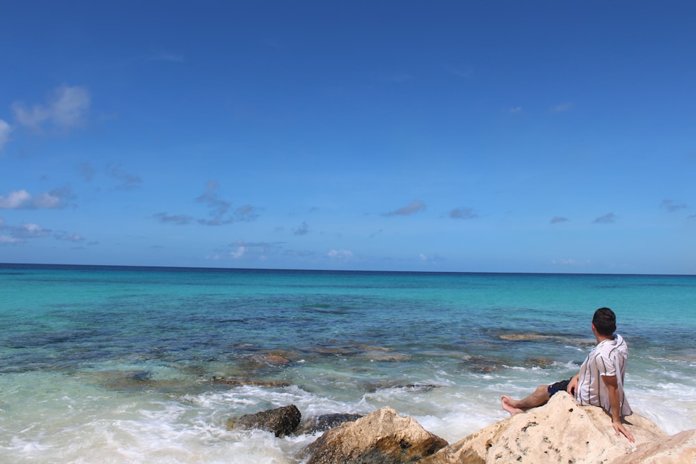 person lying on brown rock near sea under blue sky during daytime