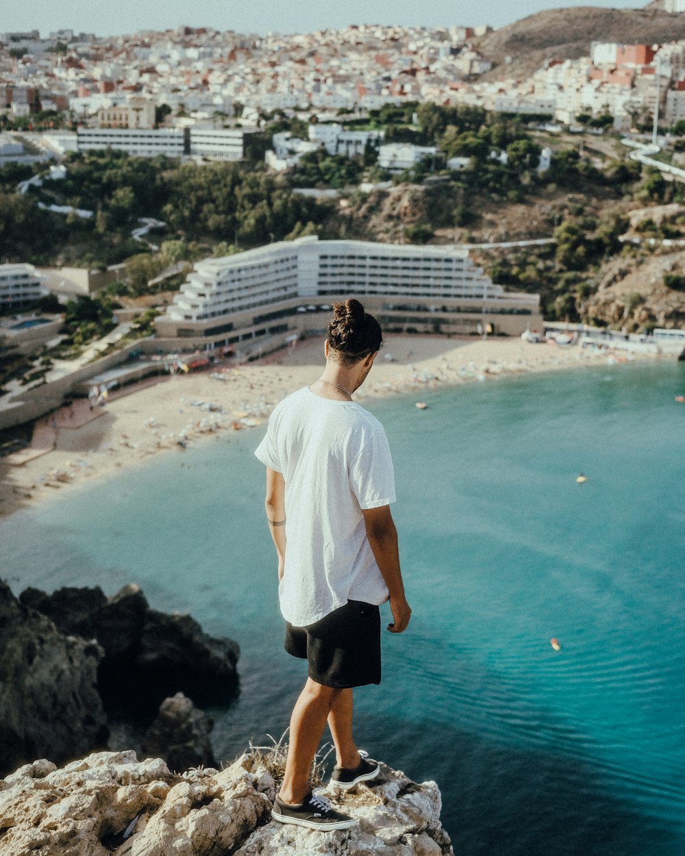 man in white shirt and black shorts standing on seashore during daytime