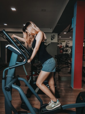 A determined woman running on a treadmill, sweat shining under warm gym lights.