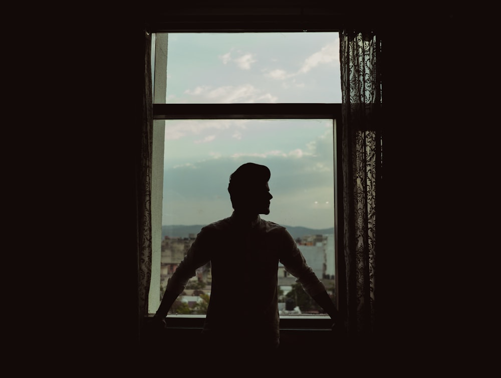 silhouette of woman standing in front of window during daytime