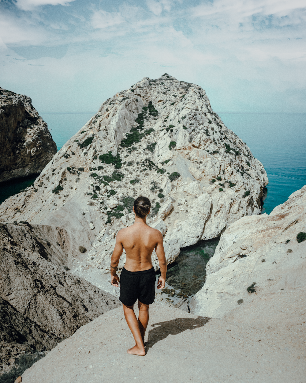 topless man in black shorts standing on rocky hill during daytime