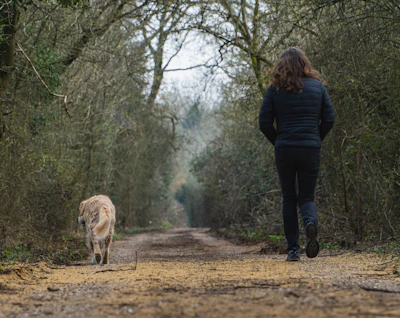 woman in blue jacket standing beside brown dog on brown field during daytime