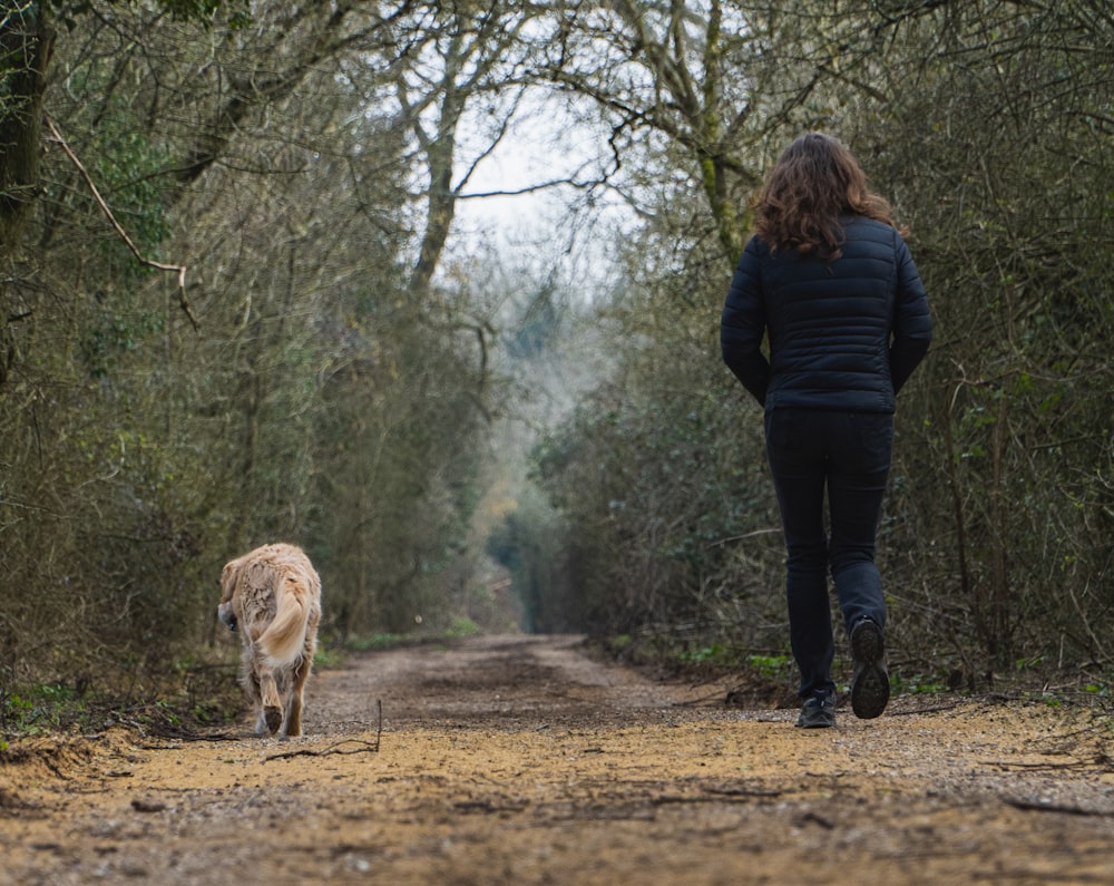 woman in blue jacket standing beside brown dog on brown field during daytime