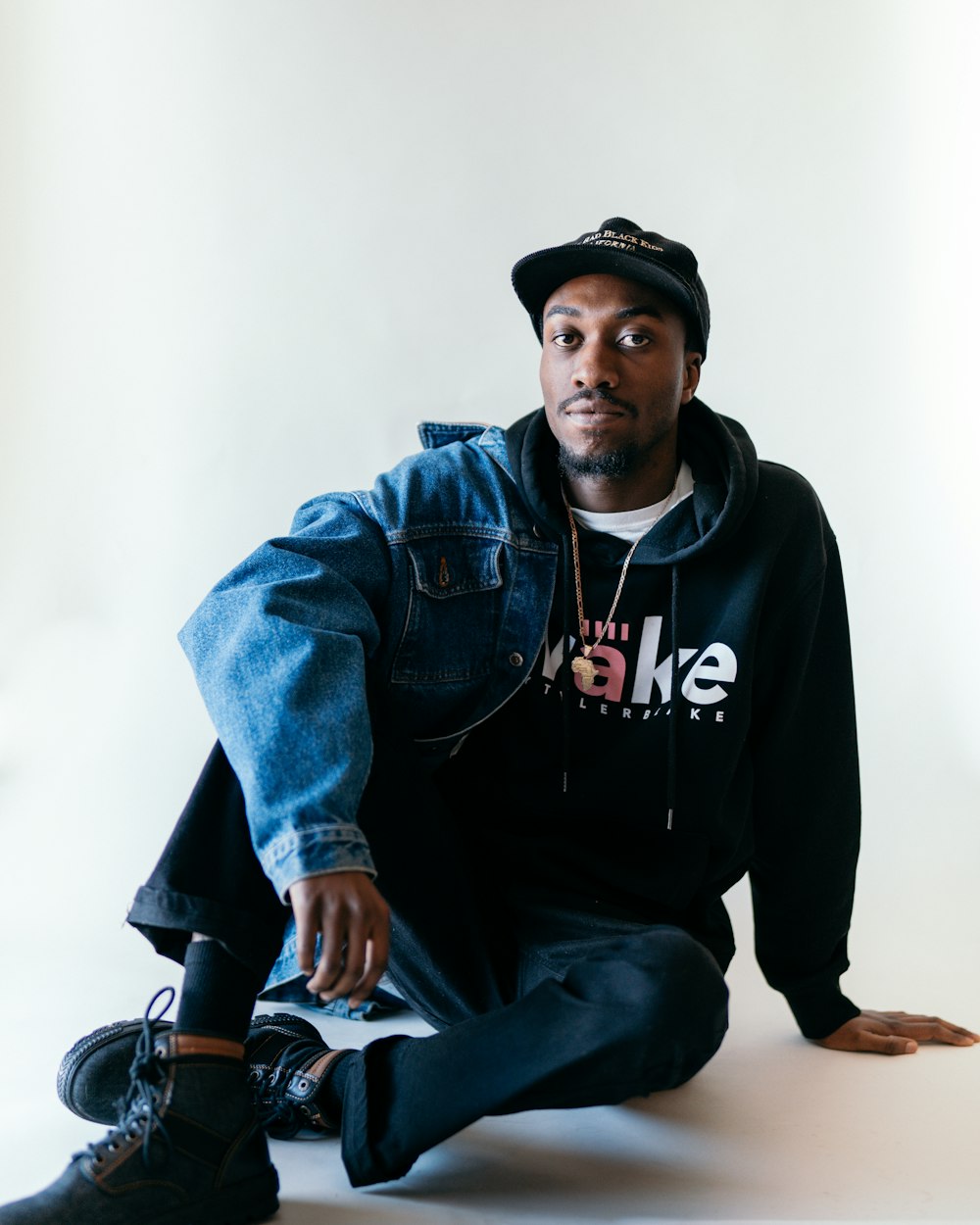 man in blue denim jacket and black fitted cap sitting on brown wooden seat