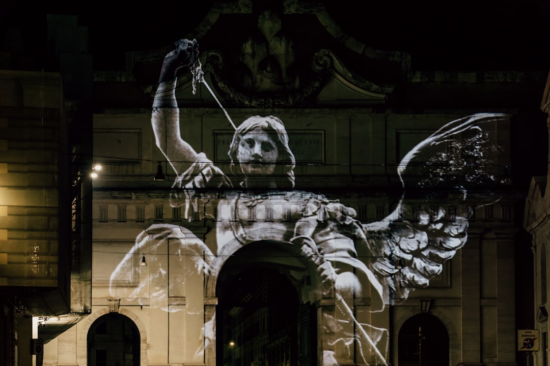 man in black jacket and pants standing on white concrete building, Angels projected onto the Porta del Popolo in Piazza del Popolo, Rome, Italy