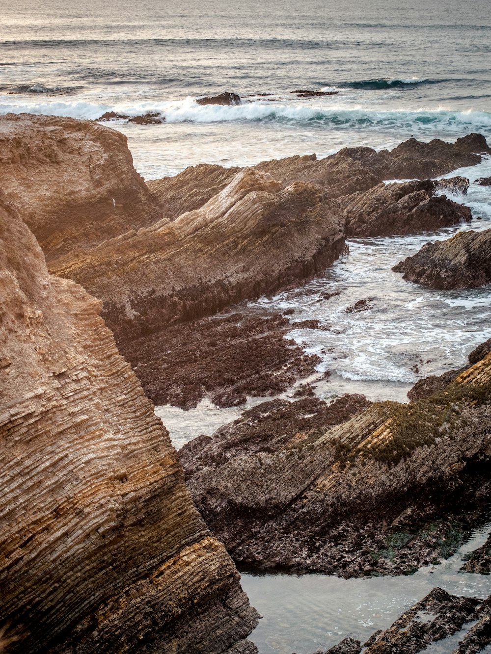 brown rocky mountain beside sea waves during daytime