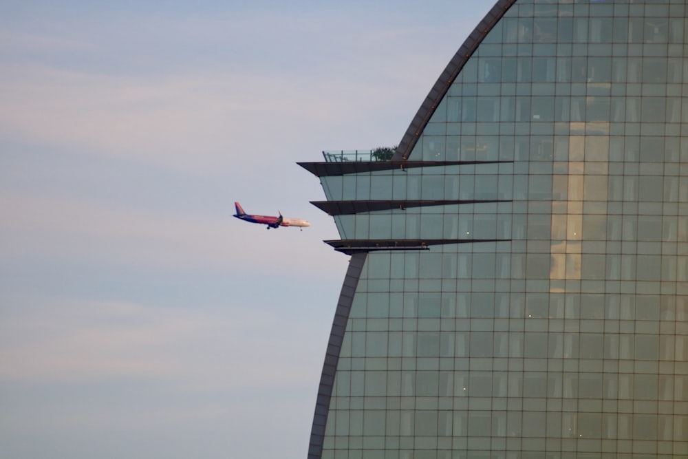 red and white plane flying over glass building during daytime
