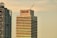 Two modern high-rise buildings with different architectural designs stand prominently. The tower on the right displays the word 'MAPFRE' on its top, with a crane visible on the roof, indicating construction or maintenance activities. The other building on the left features a unique metal frame structure on its facade.