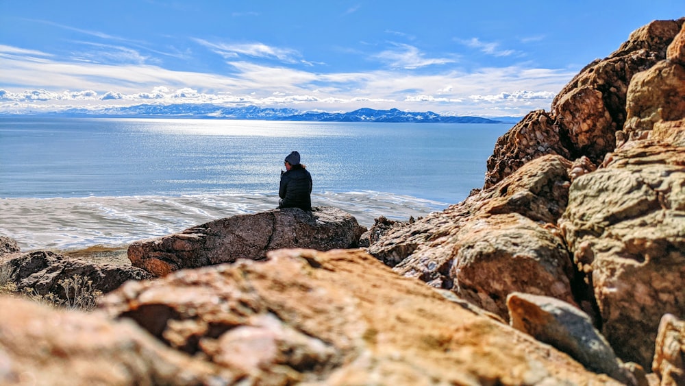 낮 동안 바다 근처 바위에 앉아 검은 재킷을 입은 남자