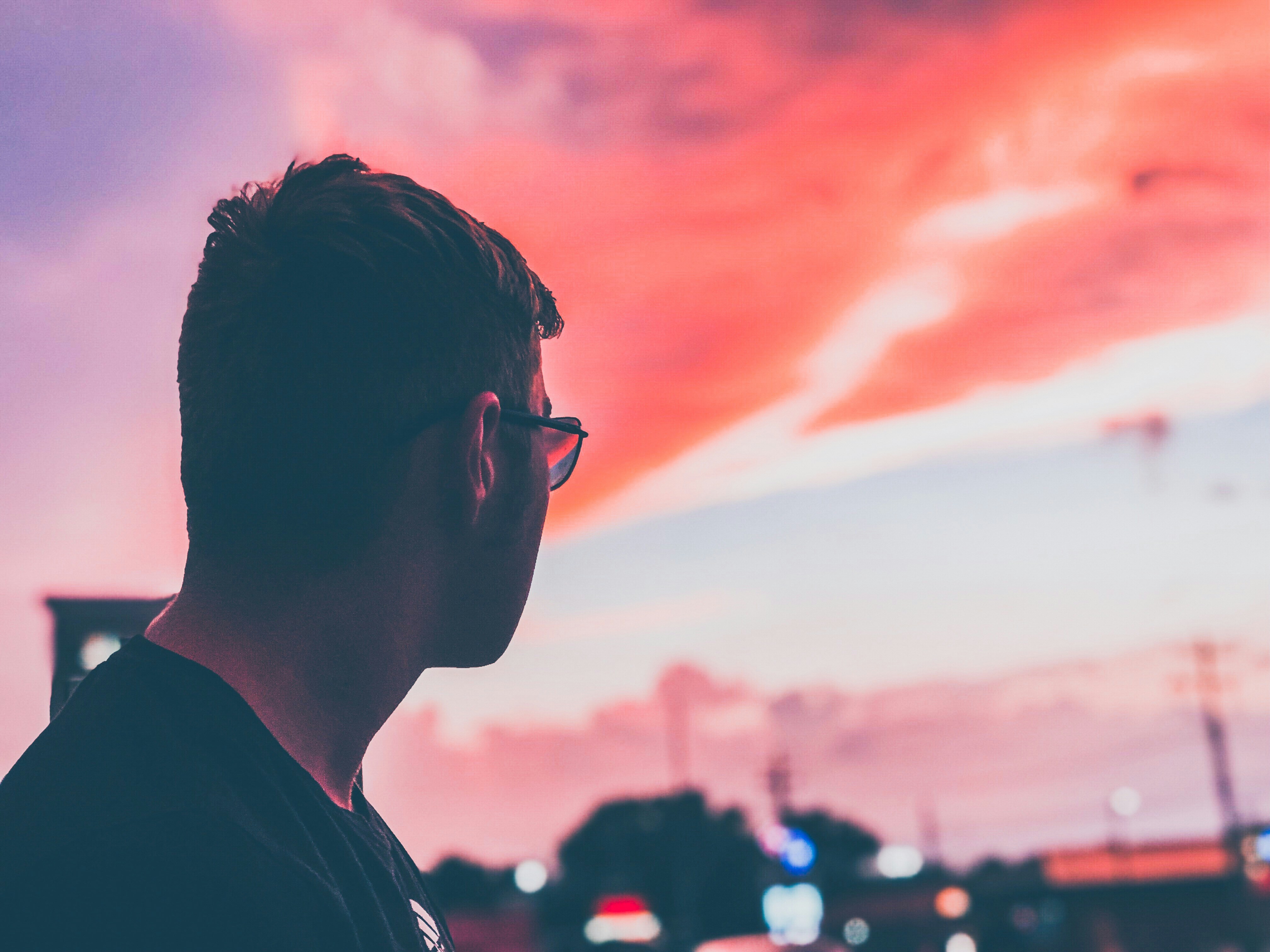 Boy in sunglasses looking off at sunset with cloudy sky in the evening.