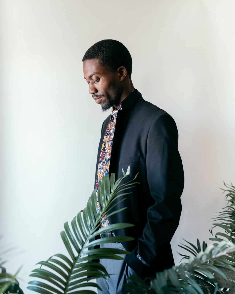 man in black suit standing near green plant